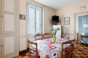 Un coin repas avec une table dressée pour quatre personnes, un téléviseur placé au-dessus de la table et une fenêtre avec des rideaux.
