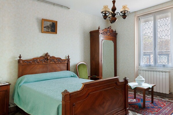 A bedroom with a wooden bed, a green chair, a mirror, and a radiator.