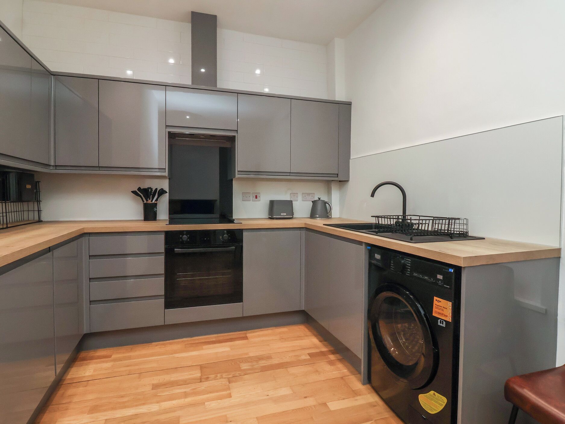 A compact kitchen with grey cabinets, a built-in oven, a dishwasher, and a wooden countertop.