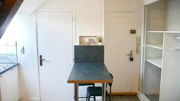 Een compacte keuken met een kleine eettafel en stoel, een witte deur en een inbouwkast.