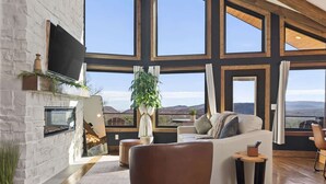Un salon spacieux doté d’une cheminée, de grandes fenêtres et offrant une vue sur les montagnes.