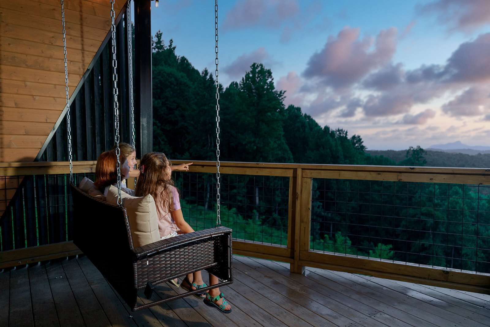 A wooden deck with a swing chair overlooking a forested landscape.