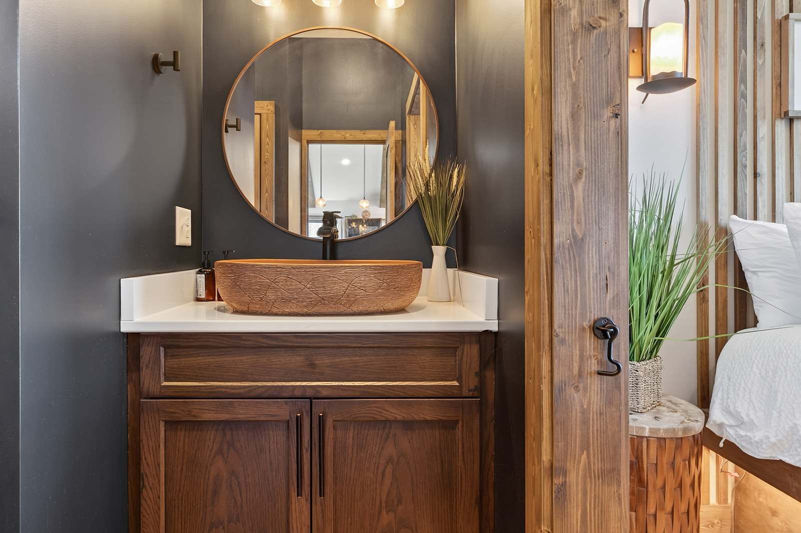 A bathroom with a wooden vanity, a round mirror, and a vessel sink.