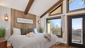 Une chambre avec un grand lit, un mur lambrissé en bois, une citation inspirante encadrée et une vue à travers une porte vitrée.