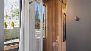 Une salle de bain moderne dotée d’une douche à parois de verre, de lambris en bois et offrant une vue sur l’extérieur.
