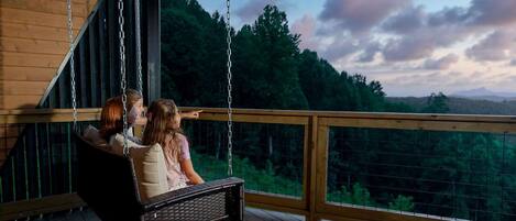A wooden deck with a swing chair overlooking a forested landscape.