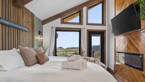 Une chambre avec un grand lit, un téléviseur fixé au mur et une vue sur l’extérieur.