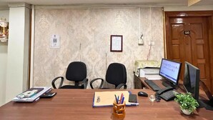 A conference room with two black office chairs, a wooden table, a desktop computer, a telephone, and a small potted plant. - YSM Grand  (Guwahati)