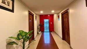 A hallway with a red wall, wooden doors, and a potted plant. - YSM Grand  (Guwahati)