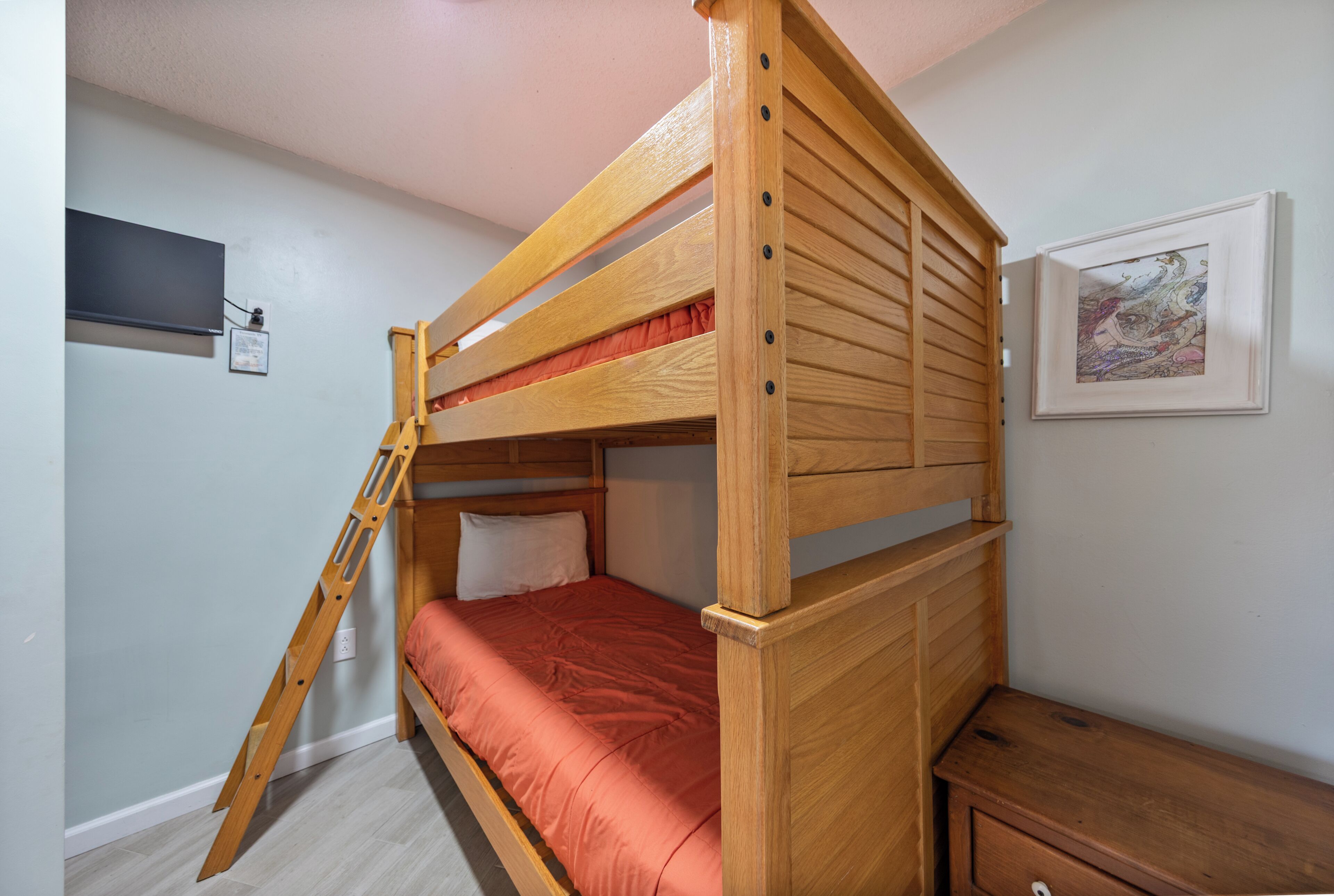 Un letto a castello con una scala, un comodino in legno e un quadro appeso al muro.