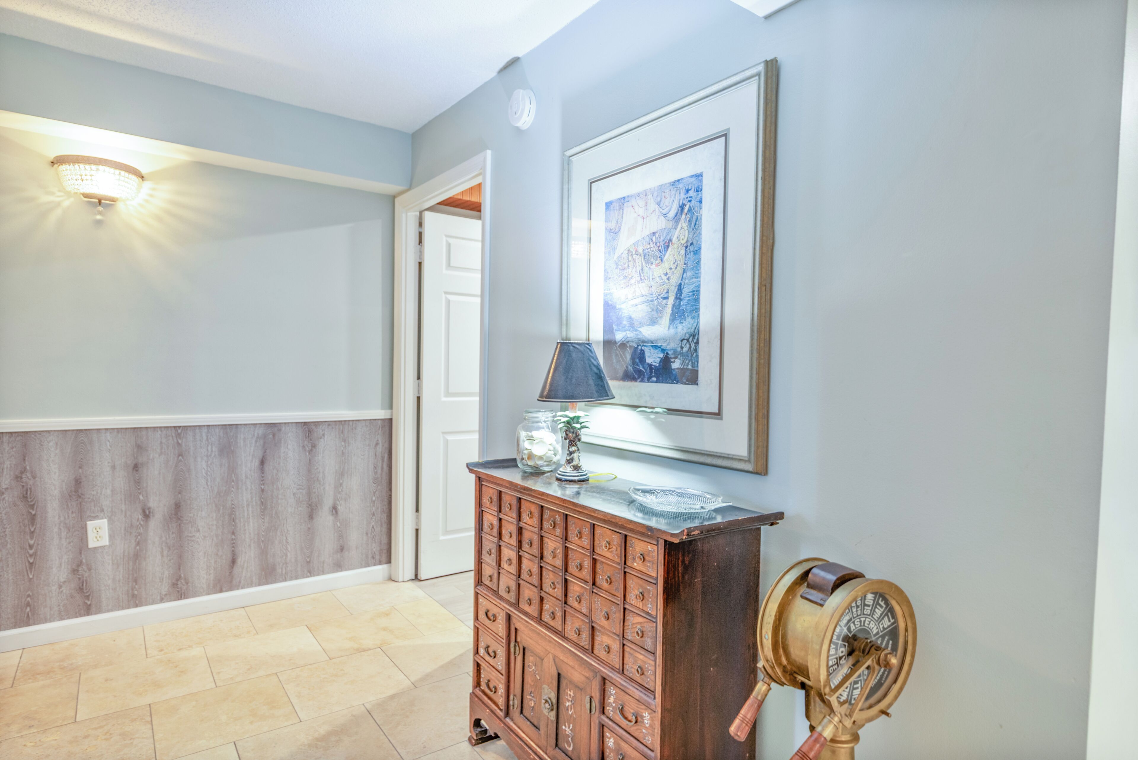 A hallway with a wooden cabinet, a framed artwork, and a vintage-style wall sconce.