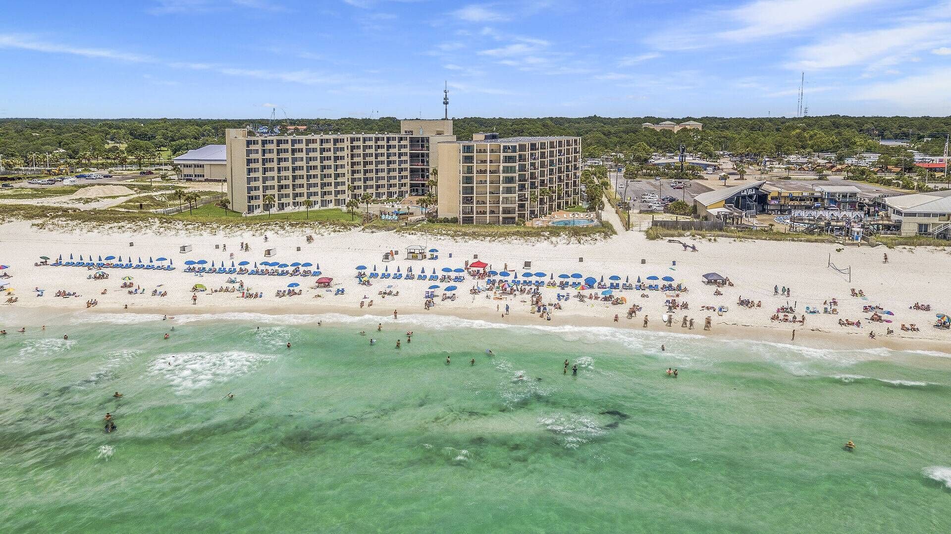 A beachfront hotel with multiple floors, a pool, and beach umbrellas.