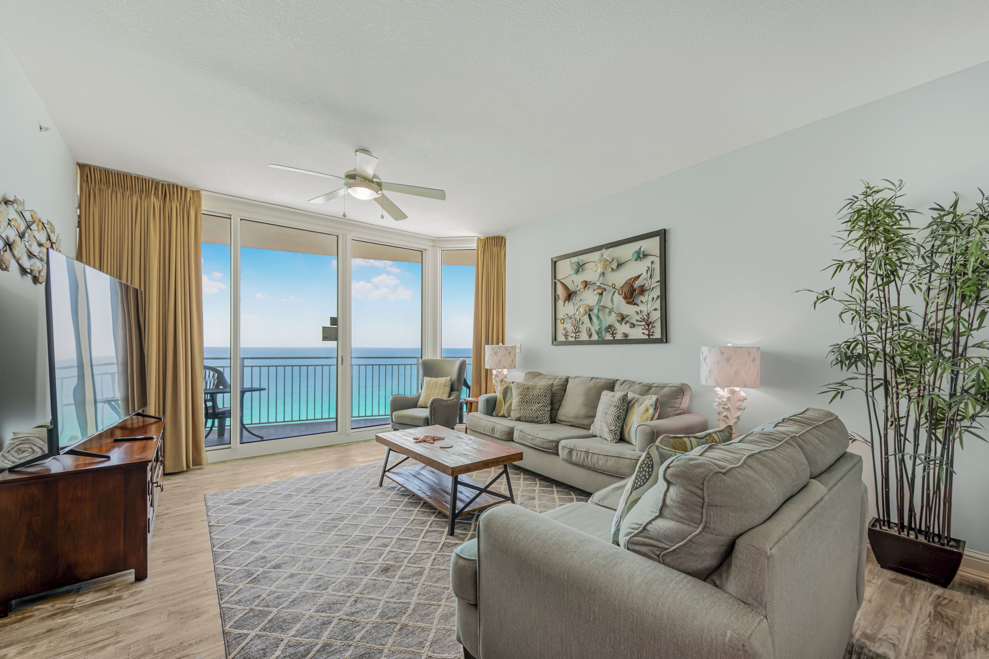 A living room with a sofa, coffee table, TV, and a large window with a view of the ocean.
