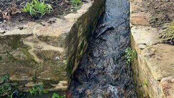 A narrow stone channel with water flowing through it, bordered by stone walls and a wooden fence.