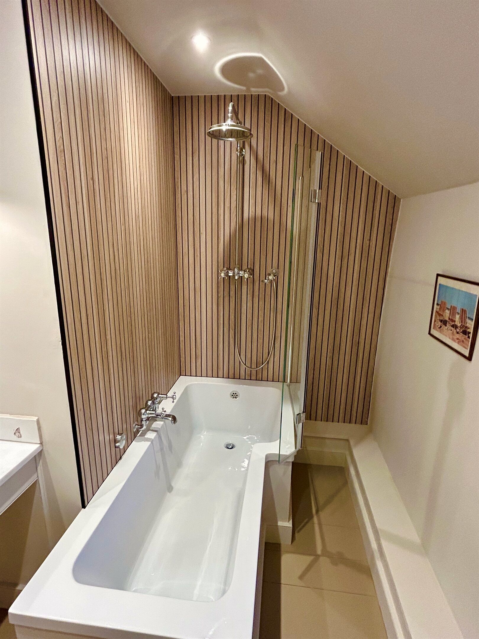 The bathroom has a large L-shaped bath with a shower over it.  