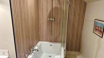 The bathroom has a large L-shaped bath with a shower over it.