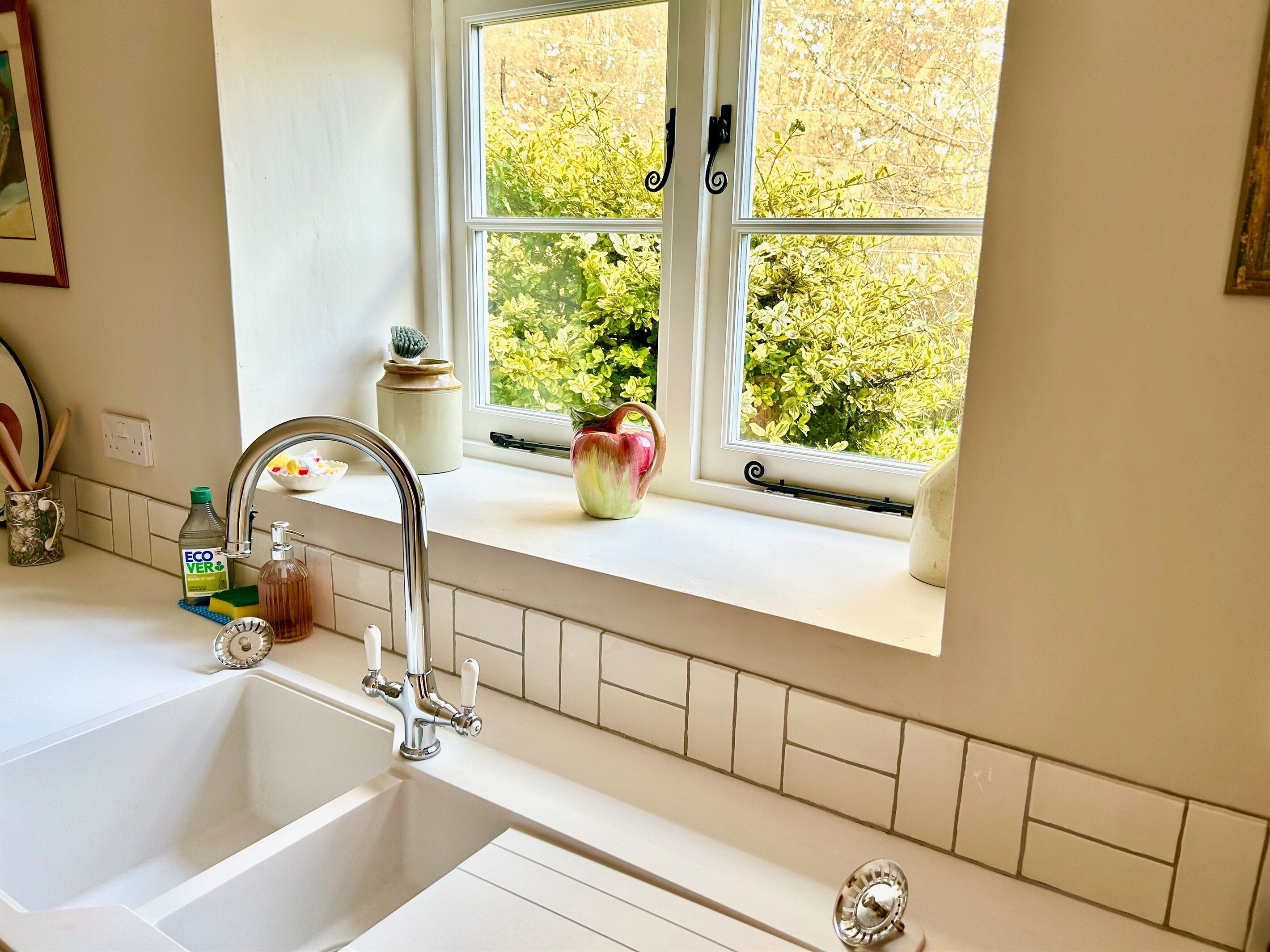 A kitchen with a double sink, a window with a view of greenery, and a vase on the windowsill.