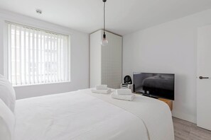 A modern bedroom with a large bed, a TV, and a window with blinds. - Spacious 2BD Flat By Docklands, Canary Wharf (Greater London)