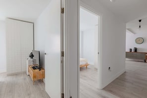 A modern, minimalist living space with a wooden floor, a white door, and a kitchen area with a clock on the wall.