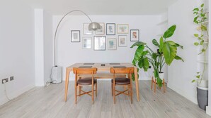 Ein Essbereich mit Holztisch und Stühlen, einer Stehlampe und gerahmten Kunstwerken an der Wand.