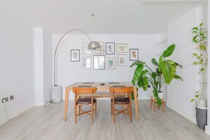 Ein Essbereich mit Holztisch und Stühlen, einer Stehlampe und gerahmten Kunstwerken an der Wand.