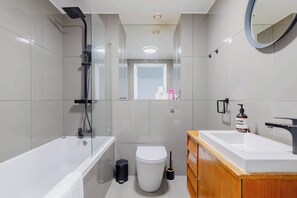 A modern bathroom with a bathtub, toilet, and sink, featuring a glass shower enclosure and a wooden vanity.