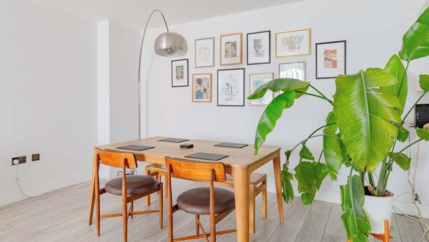 Ein Essbereich mit einem Holztisch und Stühlen, einem gerahmten Kunstwerk an der Wand und einer großen Grünpflanze.