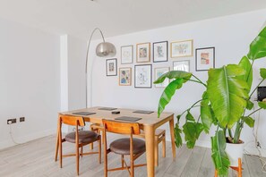 Ein Essbereich mit einem Holztisch und Stühlen, einem gerahmten Kunstwerk an der Wand und einer großen Grünpflanze.