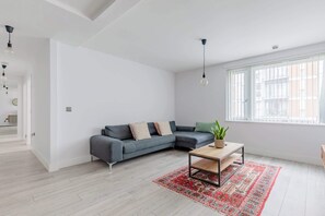 A modern living room with a grey sectional sofa, a wooden coffee table, and a red patterned rug.