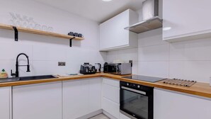 Eine moderne Küche mit weißen Schränken, einem schwarzen Geschirrspüler, einem eingebauten Backofen, einer Holzarbeitsplatte, einer Kaffeemaschine und einem Toaster.