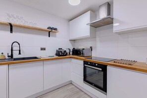 A modern kitchen with white cabinets, a black dishwasher, a built-in oven, a wooden countertop, a coffee maker, and a toaster. - Spacious 2BD Flat By Docklands, Canary Wharf (Greater London)