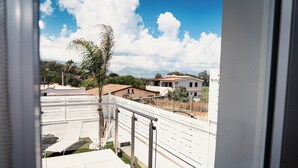 A balcony with a metal railing, a small palm tree, and a view of houses and mountains in the background. - Acqua Marina (Balestrate)