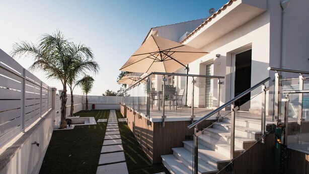 A modern outdoor area with a pathway, palm trees, and outdoor seating under umbrellas. - Acqua Marina (Balestrate)