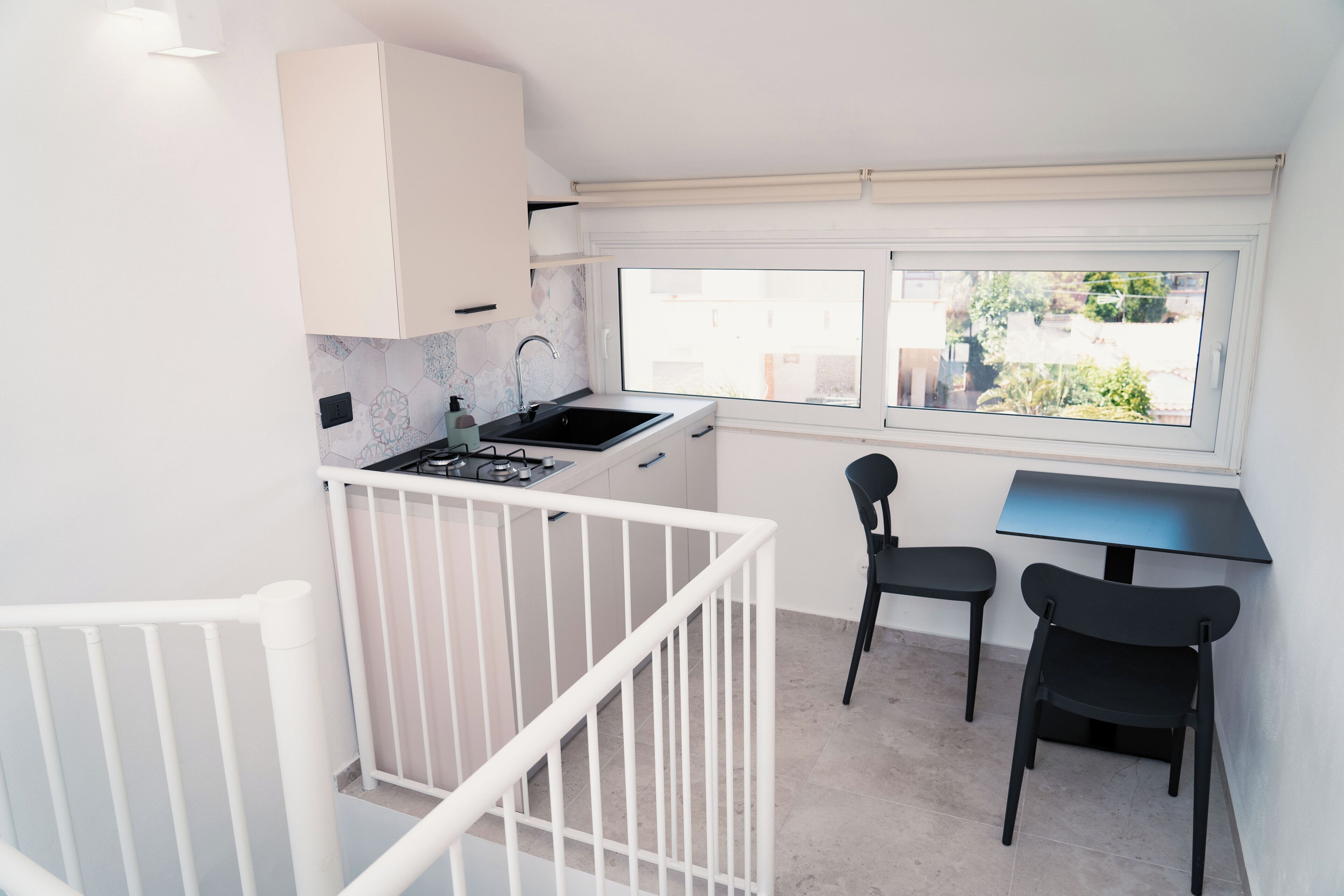 A compact kitchen with a window, a dining area with two chairs, and a white railing.