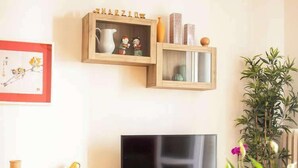 Un salon avec un téléviseur, des étagères en bois, un panier de fruits et une plante en pot.