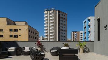 Eine Dachterrasse mit Korbmöbeln und Topfpflanzen, umgeben von modernen Gebäuden.