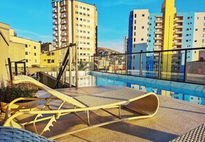 Zona de piscina en la azotea con sillones reclinables y vistas de edificios circundantes.
