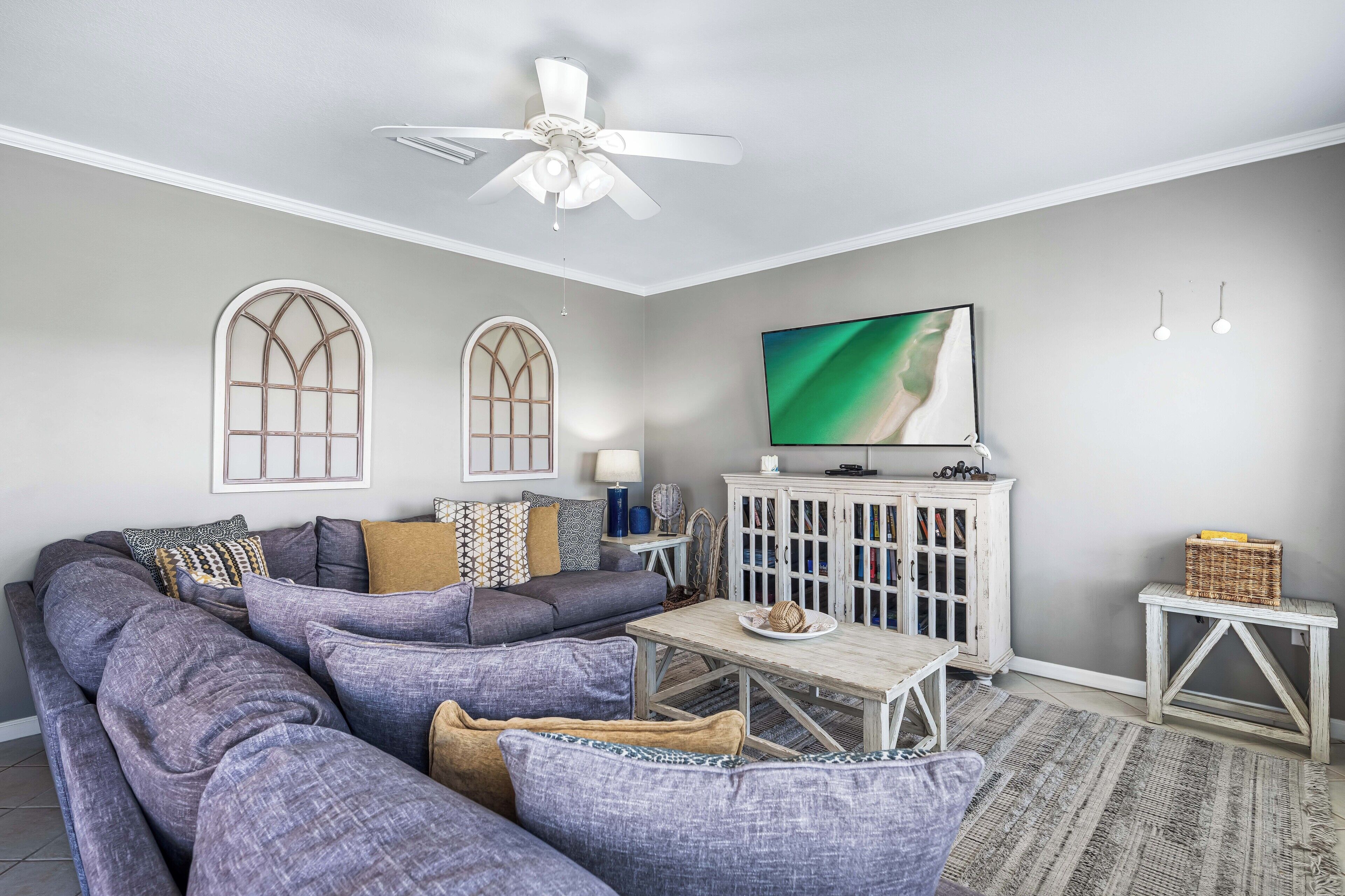 Ein Wohnzimmer mit Ecksofa, Fernseher, Deckenventilator und Schrank.