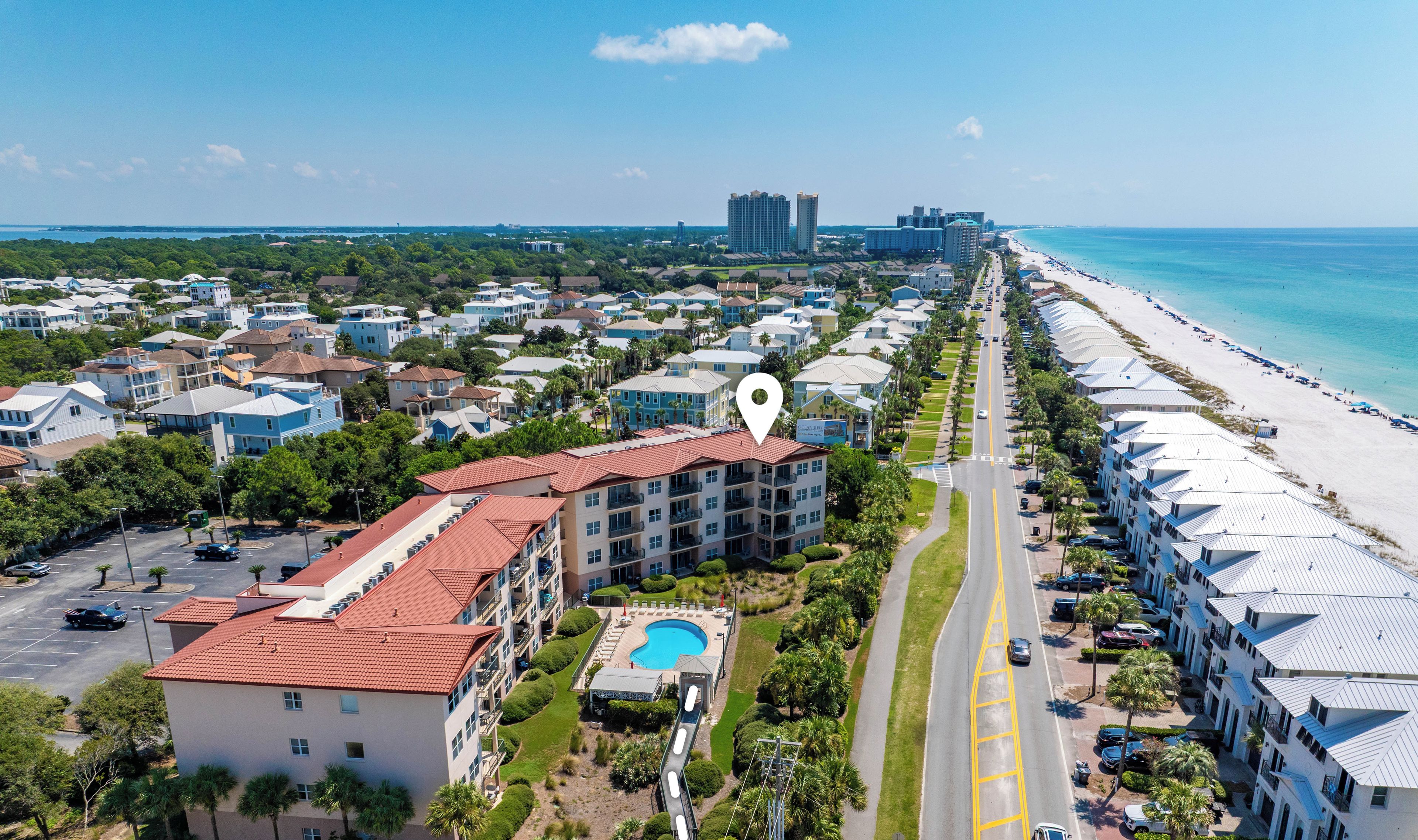 An aerial view of a coastal hotel with a swimming pool, beachfront access, and a road leading to the beach.