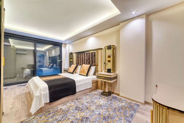 A modern hotel room with a large bed, a bedside table with a mirror, and a patterned rug.