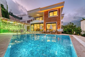 A modern two-story house with a swimming pool, outdoor seating, and a balcony.