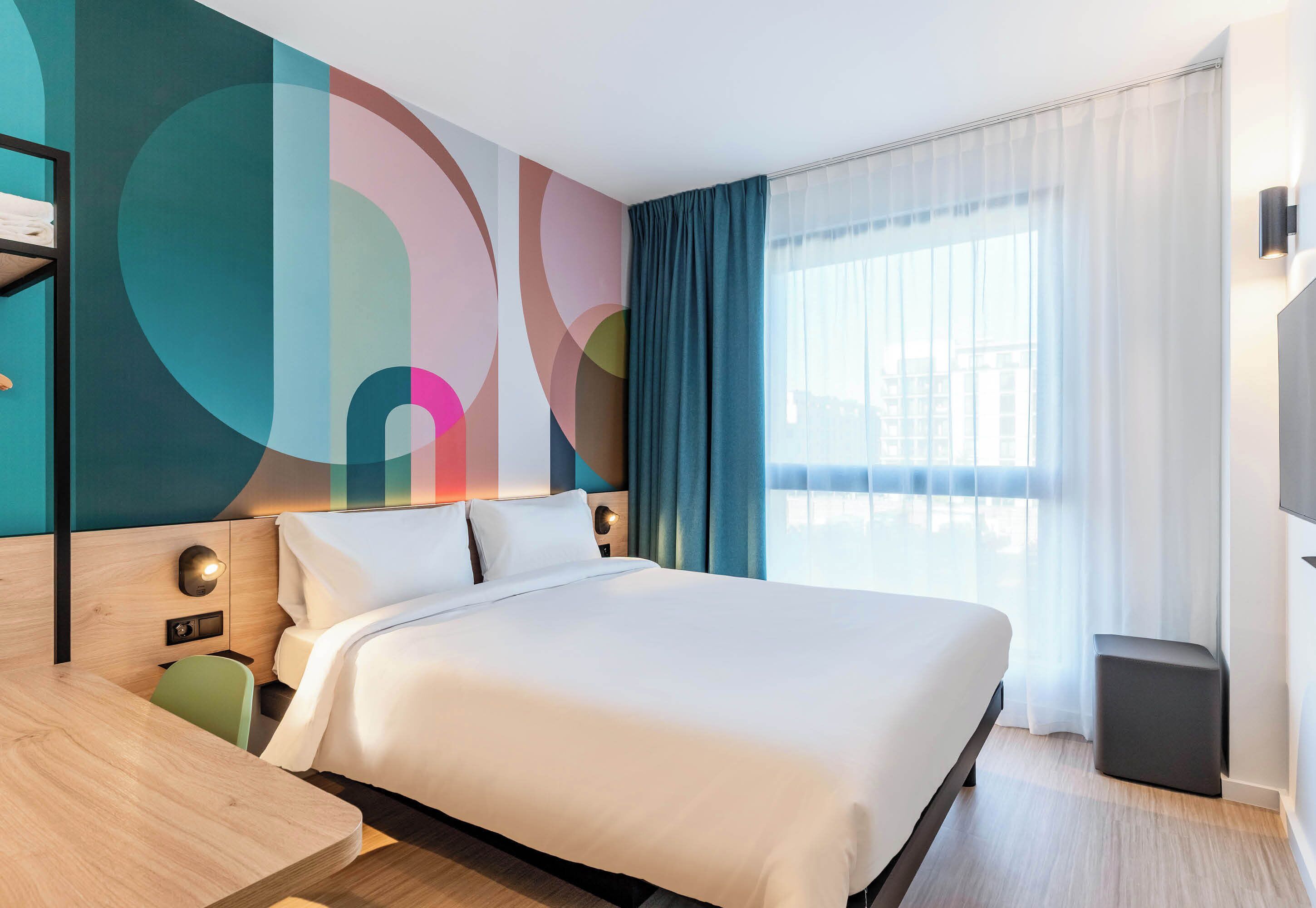 Una habitación de hotel moderna con una cama grande, un escritorio y un llamativo diseño abstracto en la pared.