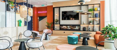A modern lounge area with seating, a television, and a 'Breakfast' sign.