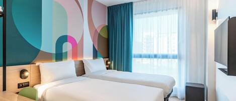 A hotel room with two beds, a desk, a TV, and a large window with curtains.
