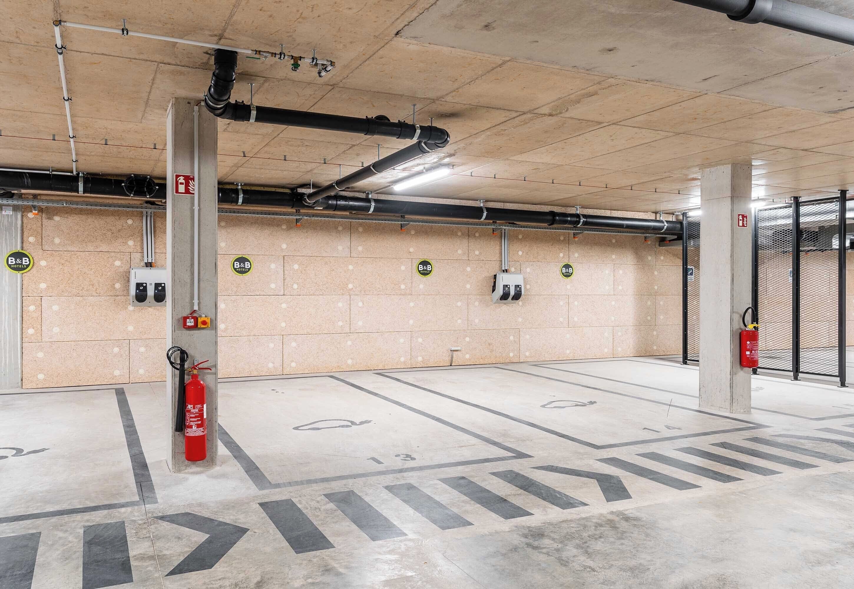 A parking garage with concrete pillars, fire extinguishers, and emergency exit signs.