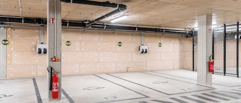 Een parkeergarage met betonnen pilaren, brandblussers en nooduitgangsborden.