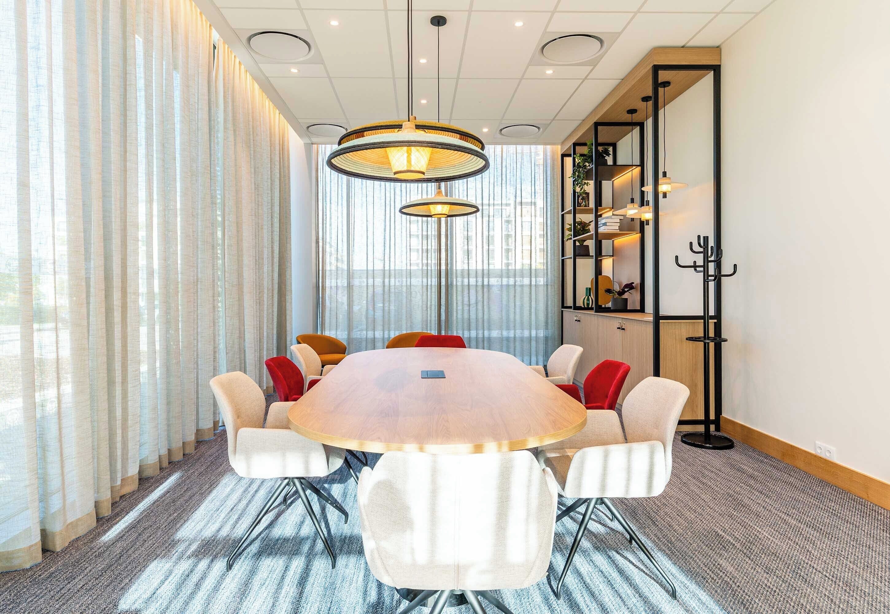 Un salón de conferencias con una mesa redonda, sillas blancas y una estantería con libros y objetos decorativos.