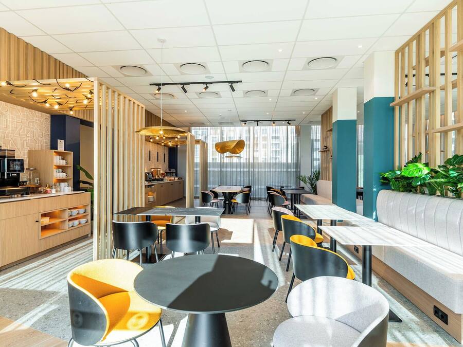 Um café moderno com área de estar central, um balcão à esquerda e uma área de estar com sofás e mesas à direita.