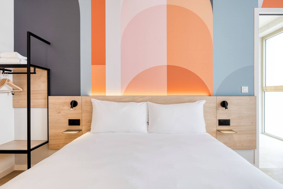 Et moderne hotelværelse med en stor seng, træsengegærde og indbyggede sengeborde.