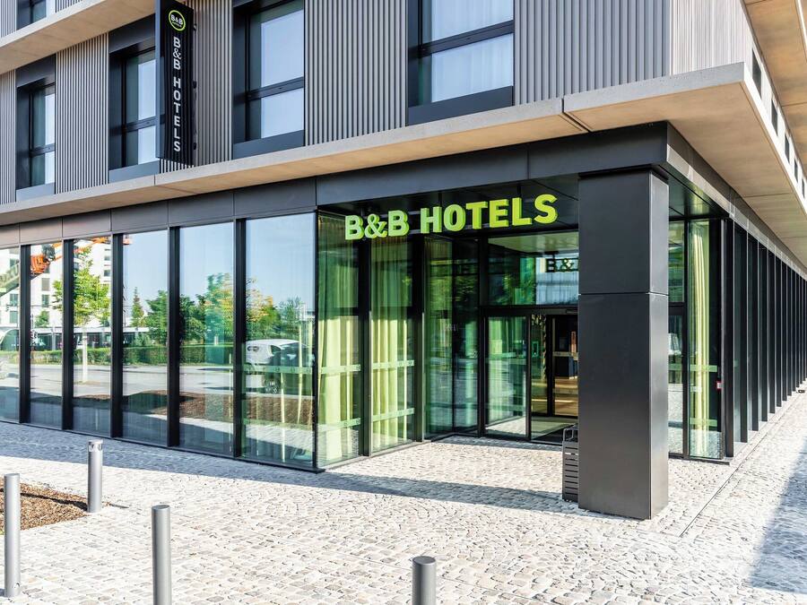 A modern B&B hotel with large glass windows and a stone-paved entrance.